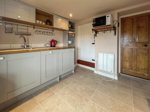 Une cuisine avec un plan de travail en bois, des placards blancs, une bouilloire rouge, un four à micro-ondes et une porte avec un panneau en bois.