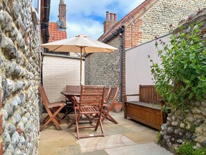 Une terrasse avec une table et des chaises, un banc en bois et un mur en pierre.