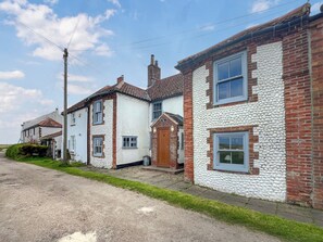Une rangée de maisons traditionnelles aux murs en briques et peints en blanc, une allée gravillonnée et un ciel dégagé.