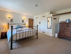 Une chambre à coucher avec un lit en métal, une commode en bois, une armoire blanche et un miroir au mur.