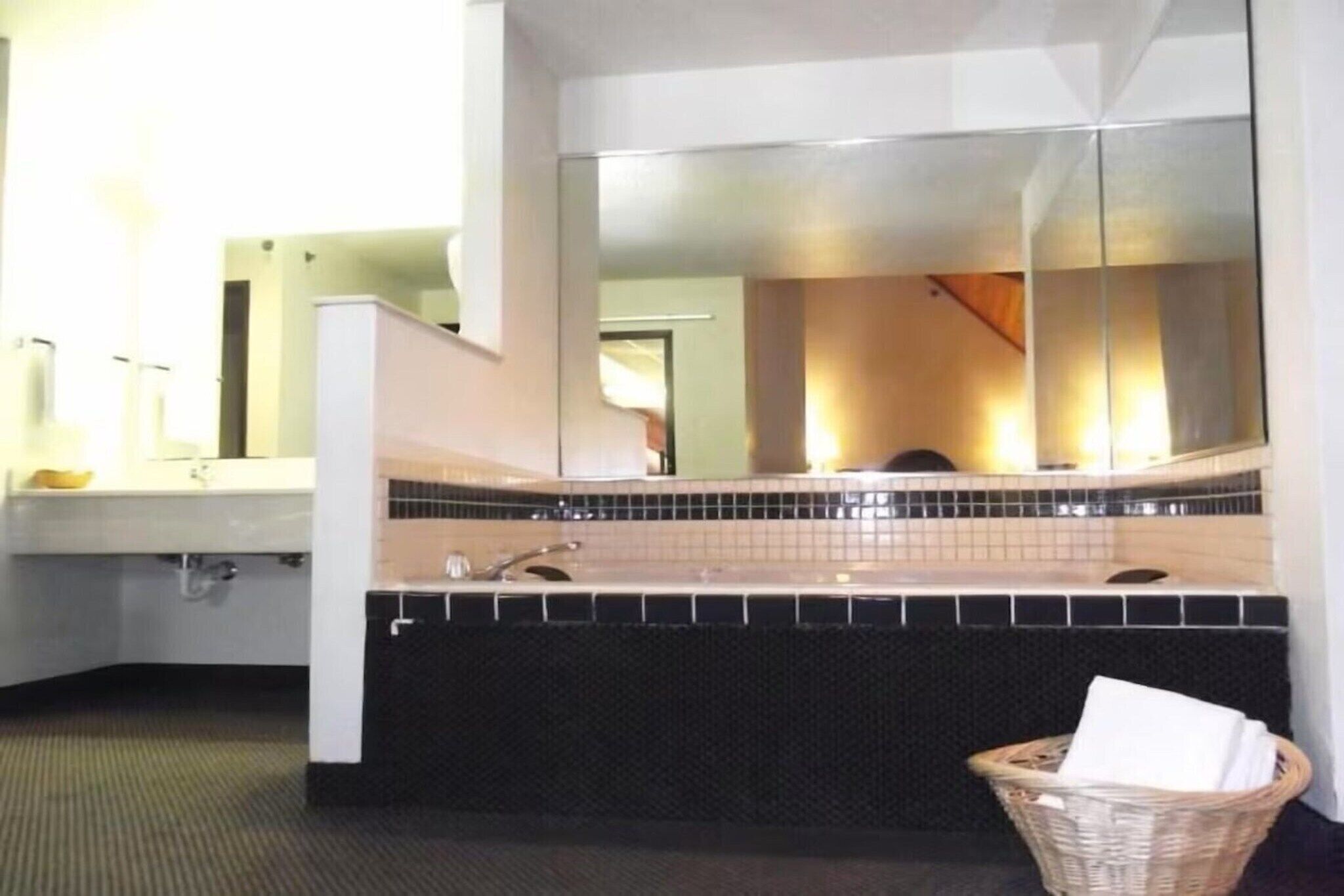 A bathroom with a large mirror, a sink, and a black textured bathtub.