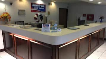A reception desk with a sign for AmeriHost Inn & Suites, a framed certificate, and a vase with flowers.