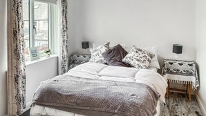 Ein Schlafzimmer mit Bett, Nachttischen, einem Fenster mit Vorhängen und Blick nach draußen.