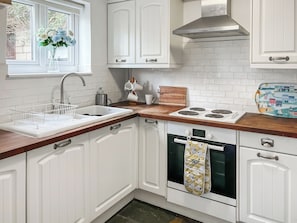 A kitchen with white cabinets, a stove, an oven, a sink with a dish rack, and a window with a vase of flowers. - 3 bedroom accommodation in Upper Rissington (Upper Rissington)