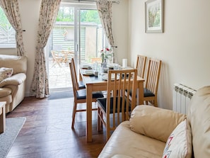 A cozy living room with a sofa, a dining table with chairs, and a view through a glass door to an outdoor area with a garden. - 3 bedroom accommodation in Upper Rissington (Upper Rissington)