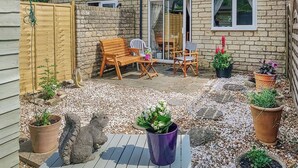 Eine Terrasse mit Holztisch und -stühlen, umgeben von Kübelpflanzen und einer Steinmauer.