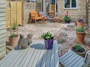 A patio with a wooden table and chairs, surrounded by potted plants and a stone wall. - 3 bedroom accommodation in Upper Rissington (Upper Rissington)