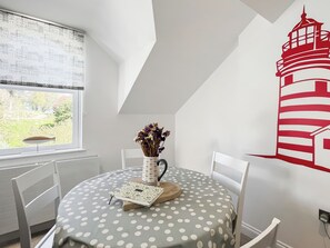Un comedor con una mesa para dos, un florero con flores y un mural en la pared de un faro.