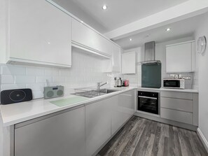 Una cocina moderna con armarios blancos, microondas, cafetera y escurreplatos.