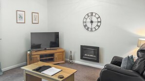Un salon avec un téléviseur, une cheminée, une horloge et un canapé.