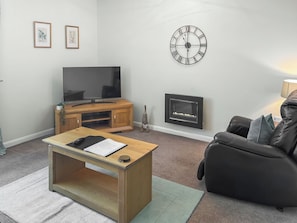 Ein Wohnzimmer mit Fernseher, Kamin, einer Uhr und einem Sofa.
