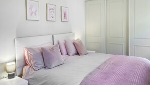 Un lit bien fait, recouvert d’une couverture rose, une lampe de chevet et une table de chevet avec des tiroirs.