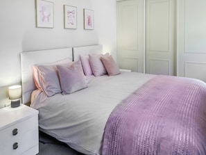 Ein ordentlich gemachtes Bett mit einer rosa Decke, einer Nachttischlampe und einem Nachttisch mit Schubladen.