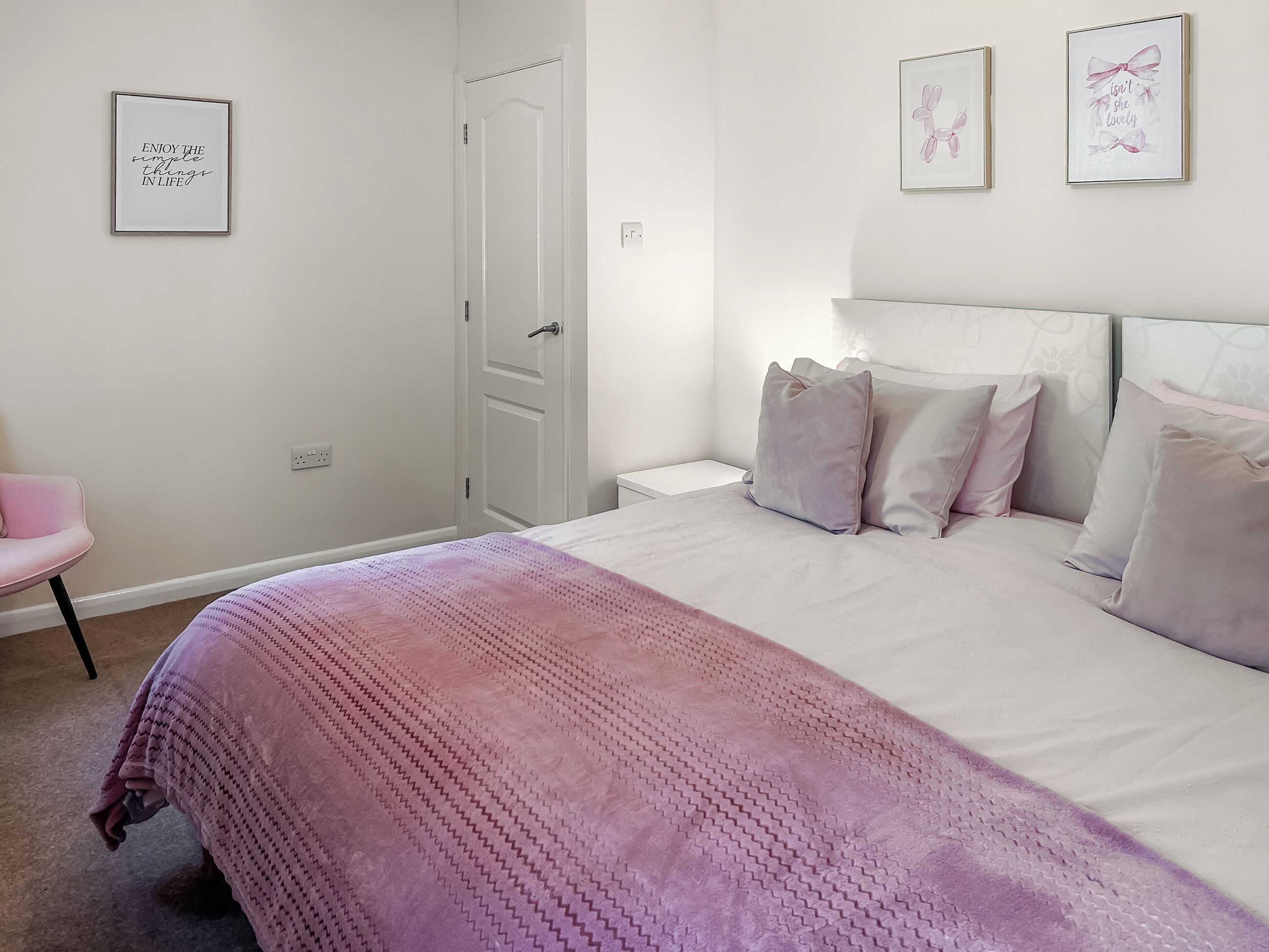 A bedroom with a bed, pillows, a chair, and wall art.