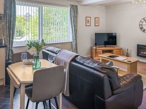 A living room with a sofa, a dining table with chairs, a TV, and a fireplace. - Beech Retreat - UK51923 (Ambleside)