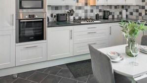 Une cuisine moderne avec des meubles blancs, un four Bosch, une cuisinière à gaz et un dosseret carrelé.