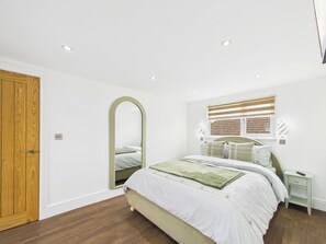 A bedroom with a bed, a mirror, a window with blinds, a bedside table, and a wooden door. - 4 bedroom accommodation in Whitstable (Whitstable)