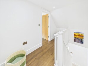 A hallway with wooden flooring, white walls, a wooden door, and a white railing with a picture. - 4 bedroom accommodation in Whitstable (Whitstable)