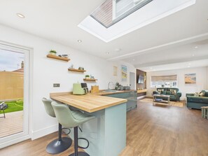 A modern kitchen with a central island, bar stools, and a dining area with a sofa and coffee table. - 4 bedroom accommodation in Whitstable (Whitstable)