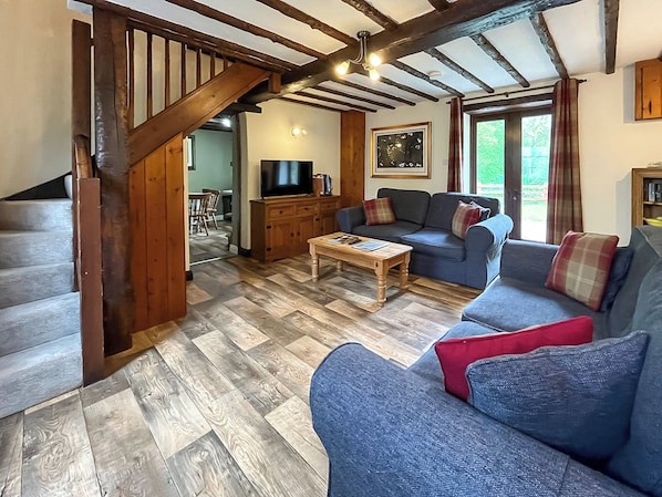 A living room with a wooden staircase, a television, a sofa, and a coffee table. - Brambles Cottage - UK51981 (Little Torrington)