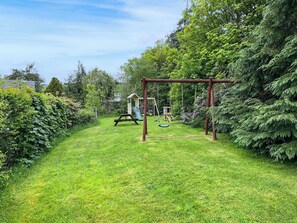 A grassy area with a swing set and a play structure. - Brambles Cottage - UK51981 (Little Torrington)
