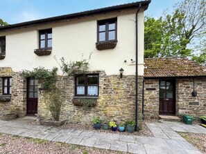 A two-story building with stone walls, multiple windows with shutters, and a tiled roof. - Otters Cottage - UK51980 (Little Torrington)