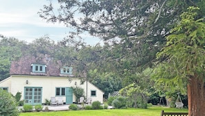 Una casa amb una porta verda, façana blanca i un jardí amb una banca.