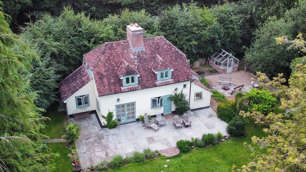 Una casa amb teules vermelles, façana blanca i un jardí amb mobiliari per a l'exterior.