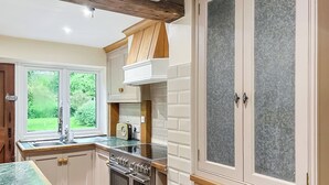 Una cuina amb forn integrat, una finestra amb vista a verdura, i un armari amb porta de malla.