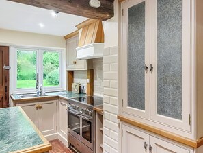 A kitchen with a built-in oven, a window with a view of greenery, and a cabinet with a mesh door.