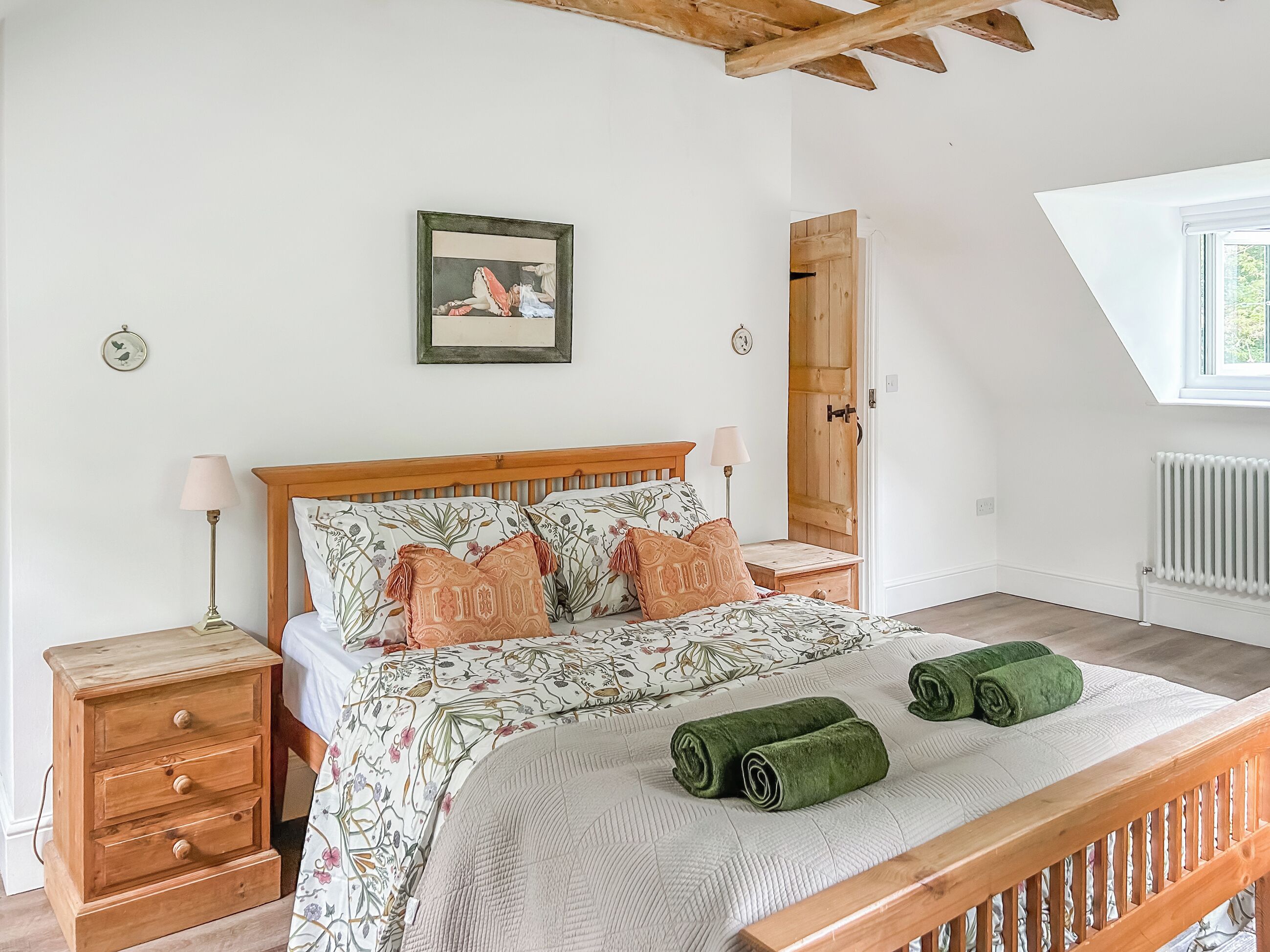 Una camera da letto con un letto di legno, due comodini, un tavolino, una porta in legno, una finestra e una sveglia a muro.