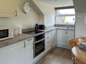 A kitchen with white cabinets, a microwave, an oven, a coffee maker, and a window with a view of buildings.
