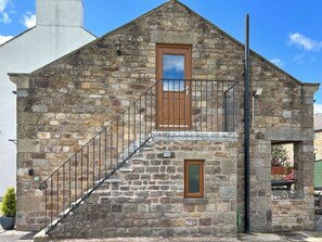 Ein Steinhaus mit einer Holztür, einem kleinen Fenster und einer Metalltreppe.