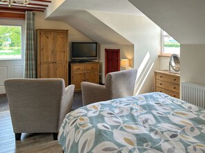 Ein Schlafzimmer mit einem Bett, zwei Sesseln, einem Fernseher, einem Holzschrank und einem Fenster mit Vorhängen.