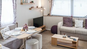 A modern living room with a sofa, a dining table set for two, a television, and a window with blinds. - 3 steps to entrance. (Rhydlewis)