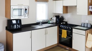 A modern kitchen with white cabinets, a black countertop, a built-in microwave, a stove, and a sink. - 3 steps to entrance. (Rhydlewis)