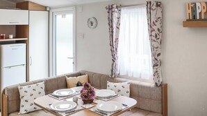A dining area with a table set for four, a sofa, a refrigerator, and a window with floral curtains. - 3 steps to entrance. (Rhydlewis)