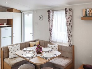 Ein Essbereich mit Tisch für vier Personen, einer Couch, einem Kühlschrank und einem Fenster mit floralem Vorhang.