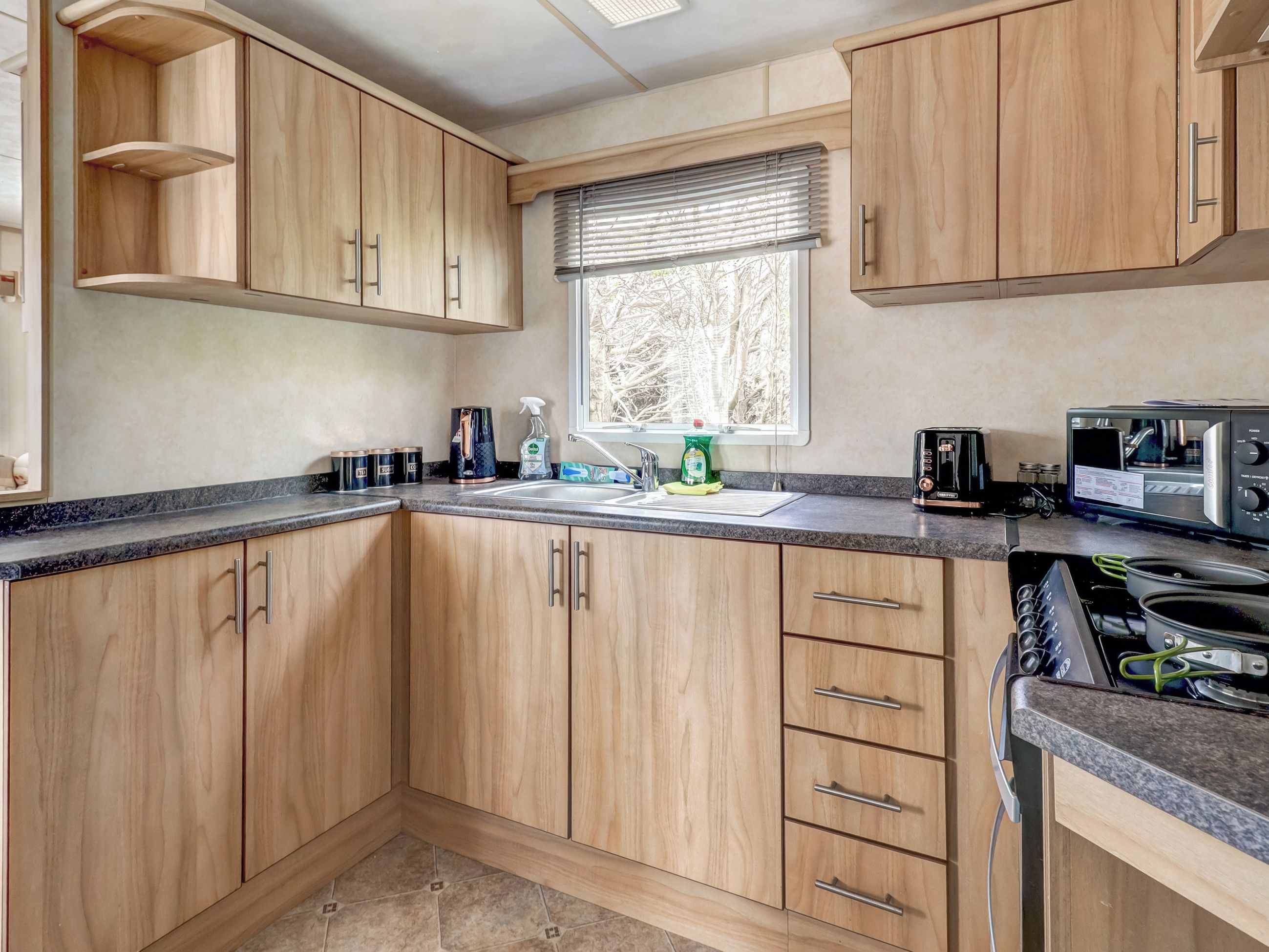 Une cuisine avec des meubles de rangement en bois, un évier, une fenêtre avec des stores et une cuisinière.