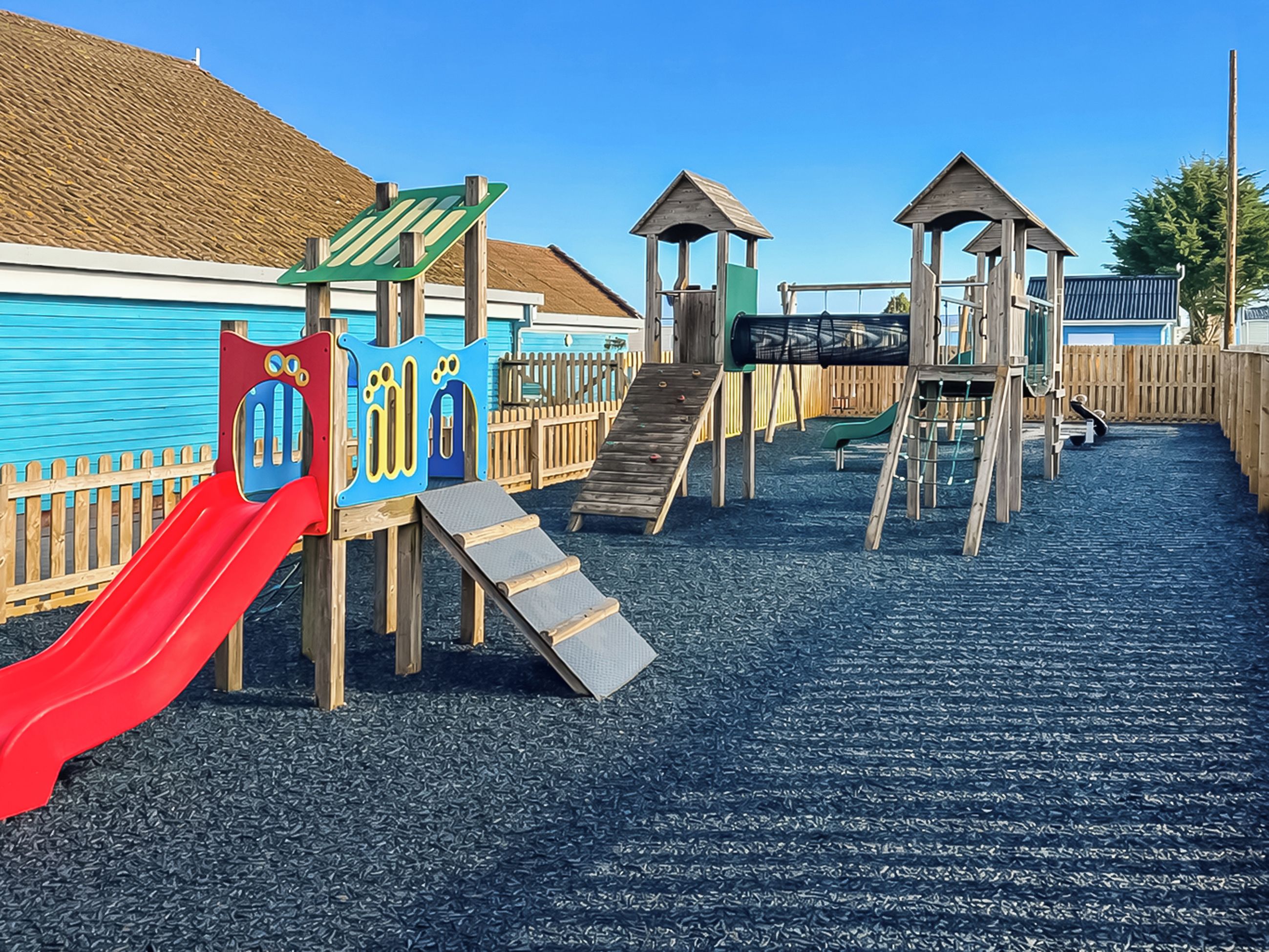 Un parque infantil con un tobogán rojo, estructuras para escalar y una valla de madera.