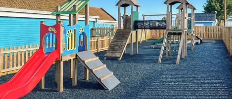 Un parque infantil con un tobogán rojo, estructuras para escalar y una valla de madera.