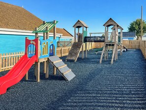 A playground with a red slide, climbing structures, and a wooden fence. - 2 bedroom accommodation in Hayling Island (Hayling Island)
