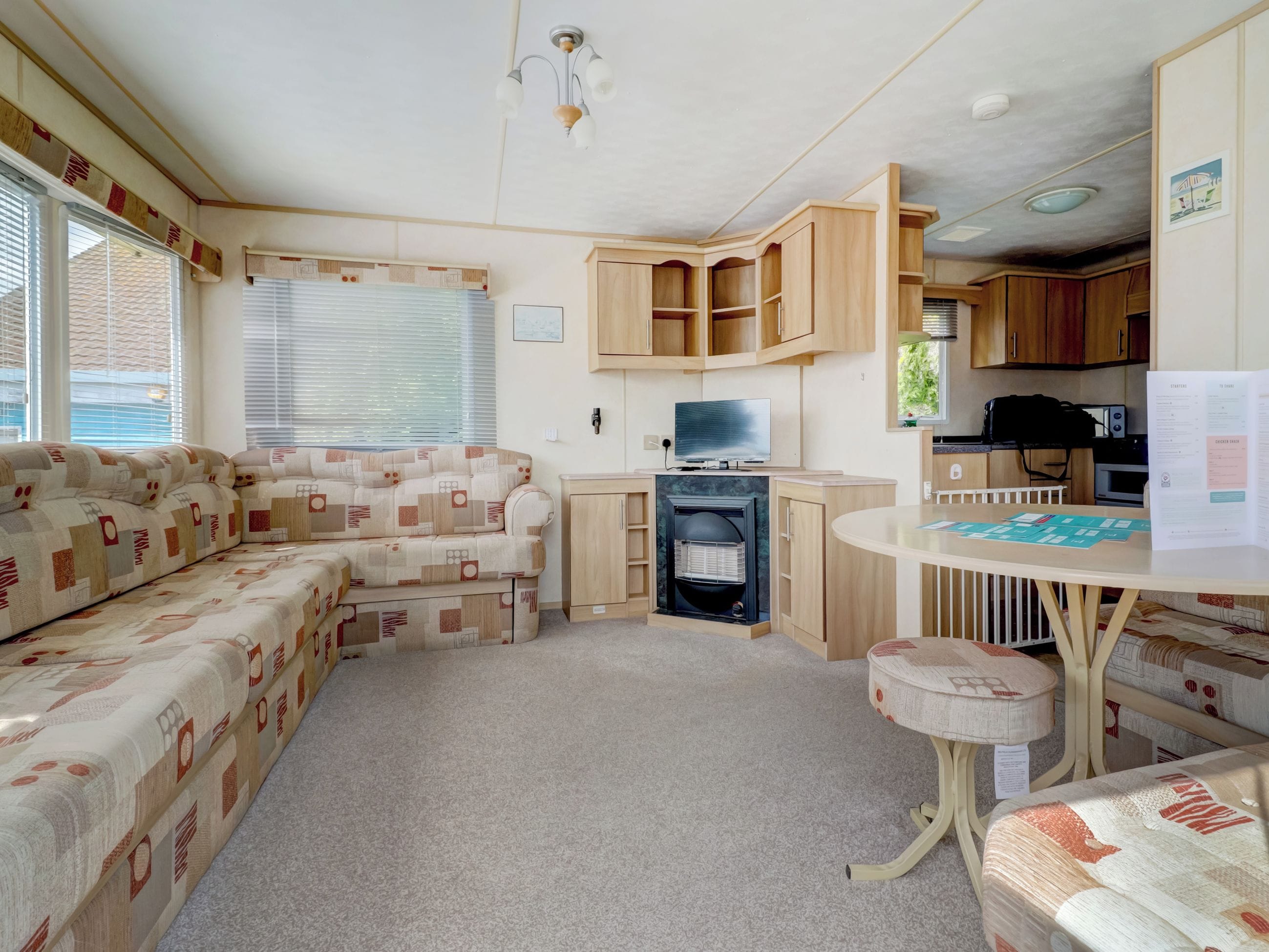 A caravan interior with a sofa, a television, a kitchen area, and a table with paperwork.