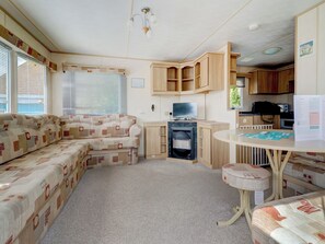 A caravan interior with a sofa, a television, a kitchen area, and a table with paperwork. - 2 bedroom accommodation in Hayling Island (Hayling Island)