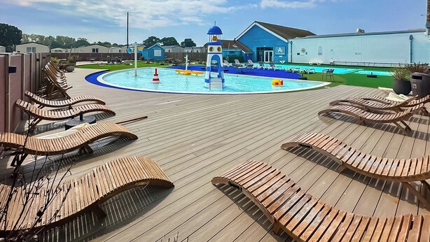 A pool area with lounge chairs, a water slide, and a building with a blue facade. - 2 bedroom accommodation in Hayling Island (Hayling Island)