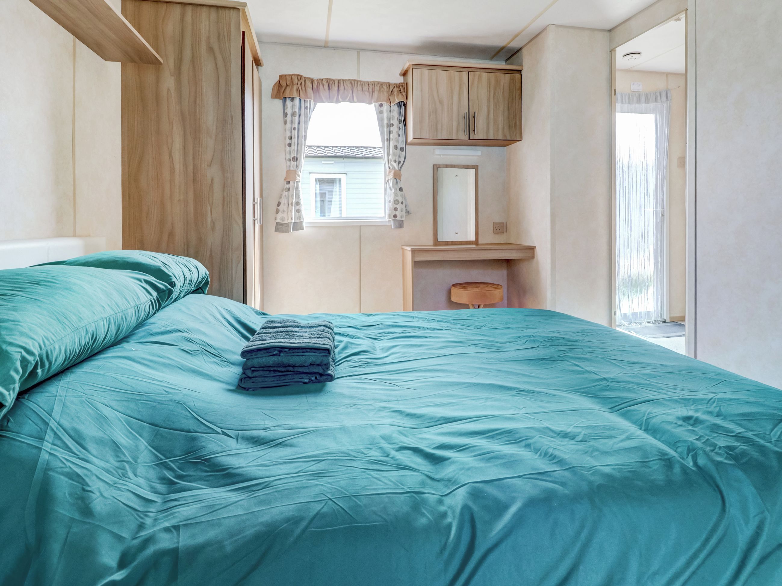 Ein Schlafzimmer mit einem Bett, einem Holzschrank, einem kleinen Tisch und einem Fenster mit Vorhängen.