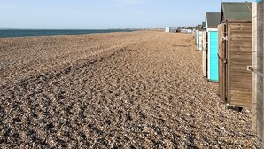 A pebble beach with wooden beach huts and a clear sky. - 2 bedroom accommodation in Hayling Island (Hayling Island)