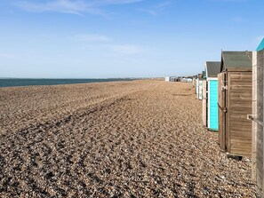 A pebble beach with wooden beach huts and a clear sky.
