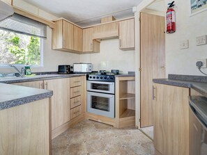 A compact kitchen with wooden cabinets, a microwave, a stove, and a fire extinguisher.