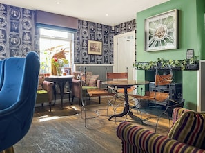 A room with a dining table, chairs, a sofa, a blue chair, and a wall with framed pictures.
